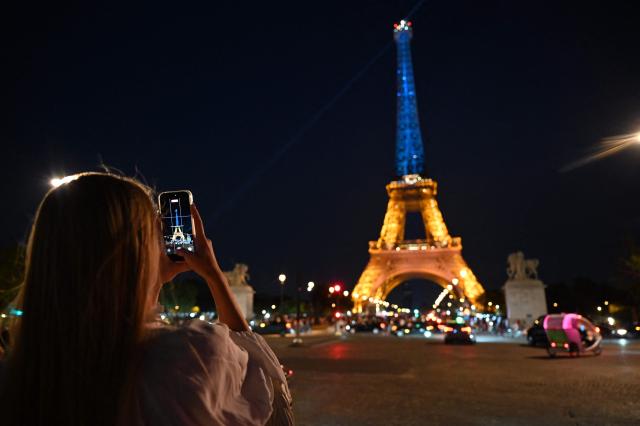 A woman takes a photograph of the Eiffel Tower as it is illuminated in the colours of the Ukrainian flag to commemorate the 35th anniversary of Ukrainian independence, in Paris, on August 24, 2026. (Photo by Christophe DELATTRE / AFP)