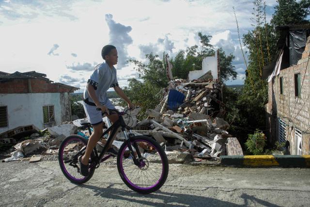 A child rides a bicycle past the rubble of a collapsed house in Buenaventura, Valle del Cauca department, Colombia, on August 24, 2026, two weeks after a magnitude 7.4 earthquake struck the area. (Photo by Cesar QUEIROZ / AFP)