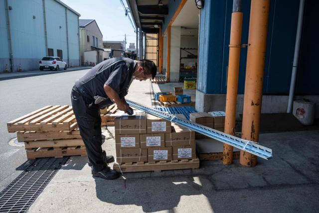 Konoe employee Isao Tabuchi scans boxes at the company's warehouse, a specialist wholesaler of screws and surveying equipment, on a hot day in Higashiosaka, Osaka Prefecture on August 21, 2026. The phonebooth-sized machine "Do Hiemon Box", where jets of ice-cold air ensure a temperature of 5C (41F), only launched this year but has proved popular in a country seemingly getting inexorably warmer. (Photo by ANDREW CABALLERO-REYNOLDS / AFP) / To go with AFP story Japan-climate-lifestyle-work, REPORTAGE by Hiroshi HIYAMA