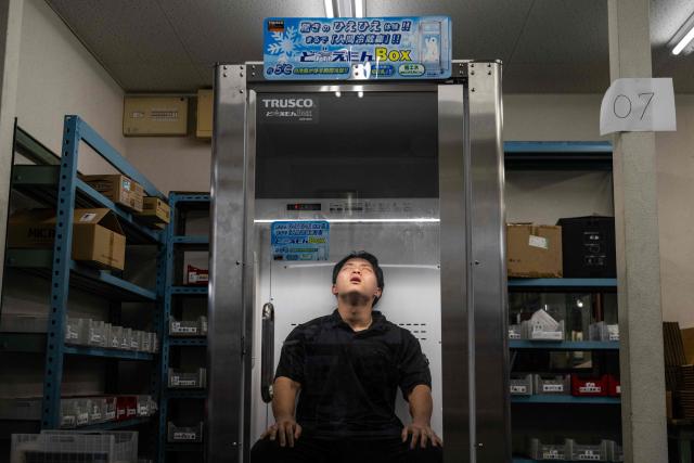 TOPSHOT - Konoe employee Taichi Konishi takes a break in a cooling box for workers also known as a "human fridge" at the company's warehouse, a specialist wholesaler of screws and surveying equipment, on a hot day in Higashiosaka, Osaka Prefecture on August 21, 2026. The phonebooth-sized machine "Do Hiemon Box", where jets of ice-cold air ensure a temperature of 5C (41F), only launched this year but has proved popular in a country seemingly getting inexorably warmer. (Photo by ANDREW CABALLERO-REYNOLDS / AFP) / To go with AFP story Japan-climate-lifestyle-work, REPORTAGE by Hiroshi HIYAMA
