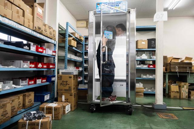 Konoe employee Taichi Konishi enters a cooling box for workers also known as a "human fridge" at the company's warehouse, a specialist wholesaler of screws and surveying equipment, on a hot day in Higashiosaka, Osaka Prefecture on August 21, 2026. The phonebooth-sized machine "Do Hiemon Box", where jets of ice-cold air ensure a temperature of 5C (41F), only launched this year but has proved popular in a country seemingly getting inexorably warmer. (Photo by ANDREW CABALLERO-REYNOLDS / AFP) / To go with AFP story Japan-climate-lifestyle-work, REPORTAGE by Hiroshi HIYAMA