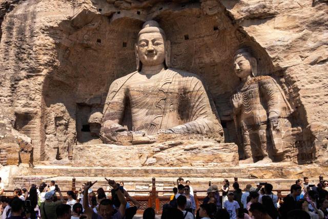 People visit a Buddha sculpture at the Yungang Grottoes in Datong, in northern China's Shanxi province on August 24, 2026. (Photo by CN-STR / AFP) / China OUT