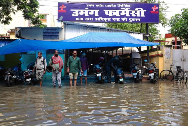 People remain stranded outside a pharmacy on a waterlogged street after heavy rain in Varanasi on August 25, 2026. (Photo by Niharika KULKARNI / AFP)