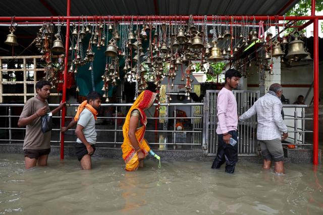 People wade through a waterlogged street in front of a temple after heavy rain in Varanasi on August 25, 2026. (Photo by Niharika KULKARNI / AFP)