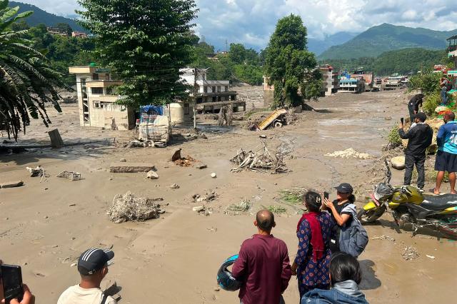 TOPSHOT - Residents look at houses partially submerged in muddy water after flash floods at Trishuli Bazar in Nepal's Nuwakot district on August 26, 2026. A massive flood swept through Nepal's northern Rasuwa district on August 26, damaging roads and power infrastructure as authorities scrambled to assess the scale of the destruction. (Photo by Prakash MATHEMA / AFP)