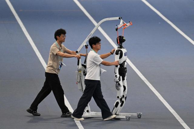 Two men prepare a humanoid robot for competition at the 2nd World Humanoid Robot Games at the National Speed Skating Oval in Beijing on August 26, 2026. (Photo by GREG BAKER / AFP)