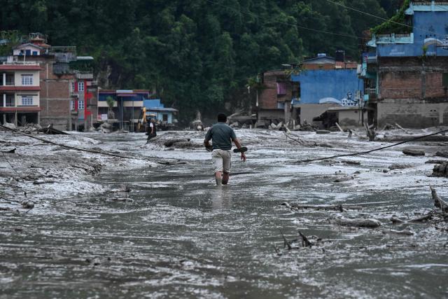 A resident walks along a street covered in mud following flash floods and a landslide disaster in Devghat, in Nepal's Nuwakot district on August 26, 2026. A massive flood and landslide disaster on the Nepal-Tibet border killed at least 103 people on August 26, 2026 and left several hundred missing, many of them foreign tourists. Aid workers said entire settlements had been "wiped out". Some 403 tourists -- 341 of them foreigners -- were unaccounted for several hours after the disaster struck, according to the tourism ministry. (Photo by PRAKASH MATHEMA / AFP)