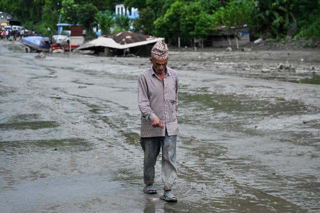 A resident walks along a street covered in mud following flash floods and a landslide disaster in Devghat, in Nepal's Nuwakot district on August 26, 2026. A massive flood and landslide disaster on the Nepal-Tibet border killed at least 103 people on August 26, 2026 and left several hundred missing, many of them foreign tourists. Aid workers said entire settlements had been "wiped out". Some 403 tourists -- 341 of them foreigners -- were unaccounted for several hours after the disaster struck, according to the tourism ministry. (Photo by PRAKASH MATHEMA / AFP)
