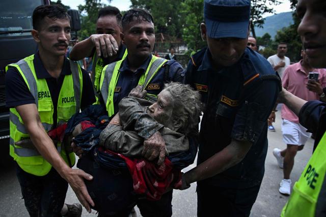 Rescuers carry in their arms a flood survivor, following flash floods and a landslide disaster in Devghat, in the Nepal's Nuwakot district on August 26, 2026. A massive flood and landslide disaster on the Nepal-Tibet border killed at least 103 people on August 26, 2026 and left several hundred missing, many of them foreign tourists. Aid workers said entire settlements had been "wiped out". Some 403 tourists -- 341 of them foreigners -- were unaccounted for several hours after the disaster struck, according to the tourism ministry. (Photo by PRAKASH MATHEMA / AFP)