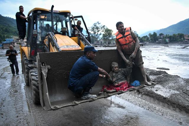 TOPSHOT - Rescuers use an excavator to transport a flood survivor, following flash floods and a landslide disaster in Devghat, in the Nepal's Nuwakot district on August 26, 2026. A massive flood and landslide disaster on the Nepal-Tibet border killed at least 103 people on August 26, 2026 and left several hundred missing, many of them foreign tourists. Aid workers said entire settlements had been "wiped out". Some 403 tourists -- 341 of them foreigners -- were unaccounted for several hours after the disaster struck, according to the tourism ministry. (Photo by PRAKASH MATHEMA / AFP)
