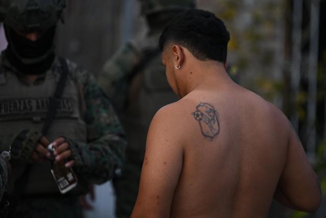 A shirtless man stands near elite members of the Ecuadorian Army during a patrol operation in the El Porvenir neighbourhood in Manta, Ecuador, on August 26, 2026. (Photo by ARIEL OCHOA / AFP)