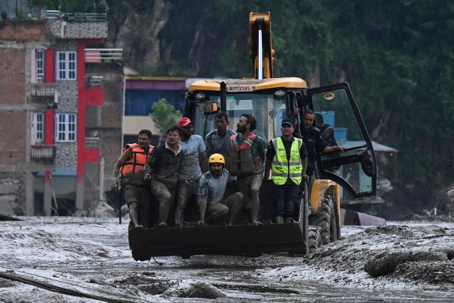 Rescuers use an excavator to transport victims and survivors along the streets submerged by mud following flash floods and a landslide disaster in Devghat in Nepal's Nuwakot district on August 26, 2026. A massive flood and landslide disaster on the Nepal-Tibet border killed at least 103 people on August 26, 2026 and left several hundred missing, many of them foreign tourists. Aid workers said entire settlements had been "wiped out". Some 403 tourists -- 341 of them foreigners -- were unaccounted for several hours after the disaster struck, according to the tourism ministry. (Photo by PRAKASH MATHEMA / AFP)