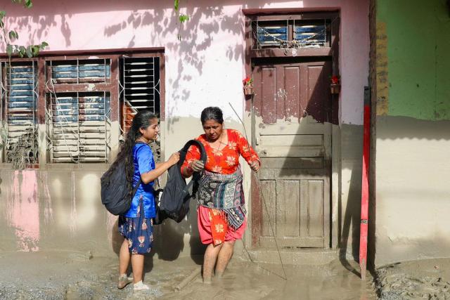 TOPSHOT - Women walk past a house bearing sludge marks that show the water level after flash floods near Devighat, Bidur Municipality in Nepal's Nuwakot district on August 27, 2026. Nepal's disaster agency said that 823 people remained out of contact on August 27, more than 24 hours after a deadly flood tore through the border region with Tibet. (Photo by Prabin RANABHAT / AFP)