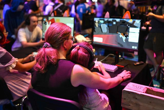 A mother and her girl play a retro video game at the Gamescom video games trade fair on the fair grounds in Cologne, western Germany, on August 27, 2026. The 2026 edition of the vast Gamescom trade fair in Cologne, Germany will be running from August 26 to 30, 2026. (Photo by Ina FASSBENDER / AFP)