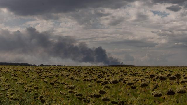 This photograph shows a sunflower field with smoke rising in the background from a warehouse following a Russian air attack near Boryspil, Kyiv region on August 27, 2026, amid the Russian invasion of Ukraine. Russia attacked Kyiv with drones on August 27, 2026, the latest in a series of increasingly frequent daytime assaults on the capital, after strikes across the country wounded around a dozen people, authorities said. (Photo by Roman PILIPEY / AFP)