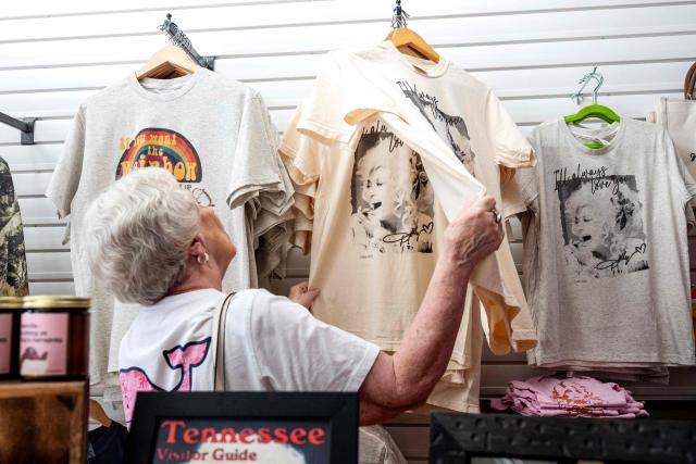 This photo taken on August 26, 2026, shows a woman browsing shirts at a gift shop across the street from the Dolly Parton Statue in Parton's hometown of Sevierville, Tennessee. Parton, the country music star who rose from grinding poverty in Tennessee to become a rhinestone-studded cultural icon with hits like "Jolene" and "9 to 5," has died at 80, her family said on August 25, 2026. Parton was more than a singer -- she wrote 3,000 songs, acted in major Hollywood films and donated millions of dollars to charities in her home state and beyond. (Photo by A.M. Stewart / AFP)