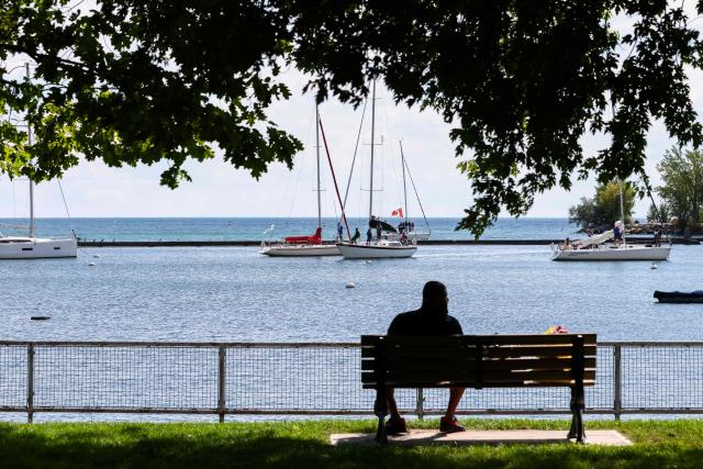A man sits on a bench in a harbor on Lake Ontario on a boardwalk in Toronto, Ontario, on August 27, 2026. US President Donald Trump announced that he is renaming Lake Ontario -- a large body of water shared by the United States and Canada -- "Lake America." Trump signed an order in the White House in a move that comes amid a spiraling trade war between the world's largest economy and its northern neighbor. (Photo by Cole Burston / AFP)