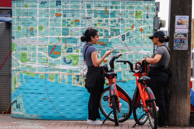 People stand beside a map of Toronto and Lake Ontario, in Toronto, Ontario, on August 27, 2026. US President Donald Trump announced that he is renaming Lake Ontario -- a large body of water shared by the United States and Canada -- "Lake America." Trump signed an order in the White House in a move that comes amid a spiraling trade war between the world's largest economy and its northern neighbor. (Photo by Cole Burston / AFP)