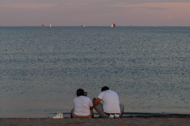 People sit in the sand on a beach at Lake Ontario in Toronto, Ontario, on August 27, 2026. US President Donald Trump announced that he is renaming Lake Ontario -- a large body of water shared by the United States and Canada -- "Lake America." Trump signed an order in the White House in a move that comes amid a spiraling trade war between the world's largest economy and its northern neighbor. (Photo by Cole Burston / AFP)