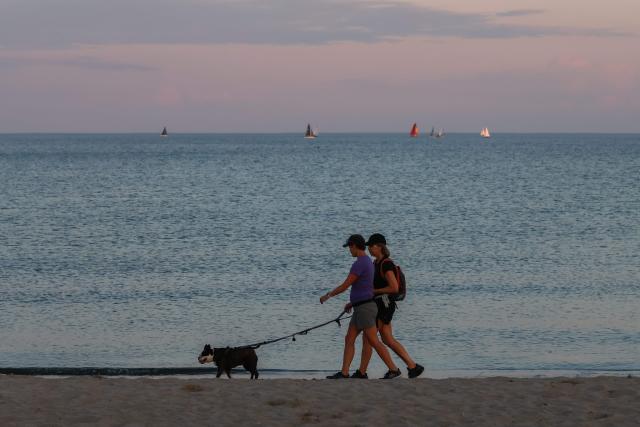 People walk a dog at dusk on the shore of Lake Ontario in Toronto, Ontario, on August 27, 2026. US President Donald Trump announced that he is renaming Lake Ontario -- a large body of water shared by the United States and Canada -- "Lake America." Trump signed an order in the White House in a move that comes amid a spiraling trade war between the world's largest economy and its northern neighbor. (Photo by Cole Burston / AFP)