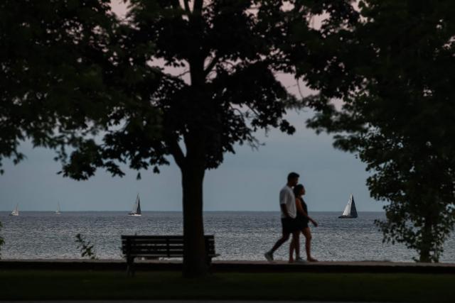 People walk at dusk near the beach on Lake Ontario in Toronto, Ontario, on August 27, 2026. US President Donald Trump announced that he is renaming Lake Ontario -- a large body of water shared by the United States and Canada -- "Lake America." Trump signed an order in the White House in a move that comes amid a spiraling trade war between the world's largest economy and its northern neighbor. (Photo by Cole Burston / AFP)