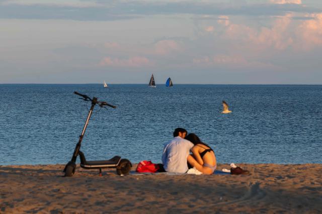 People sit in the sand on a beach at Lake Ontario in Toronto, Ontario, on August 27, 2026. US President Donald Trump announced that he is renaming Lake Ontario -- a large body of water shared by the United States and Canada -- "Lake America." Trump signed an order in the White House in a move that comes amid a spiraling trade war between the world's largest economy and its northern neighbor. (Photo by Cole Burston / AFP)