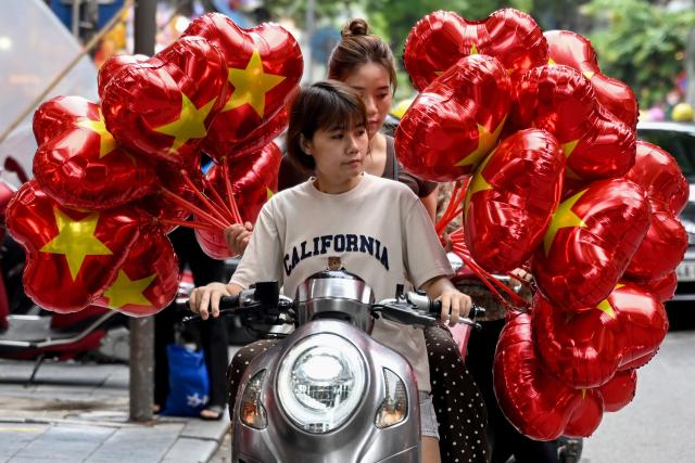 Women commute on a motorbike carrying balloons featuring the Vietnamese national flag on a street in Hanoi on August 28, 2026. (Photo by Nhac NGUYEN / AFP)
