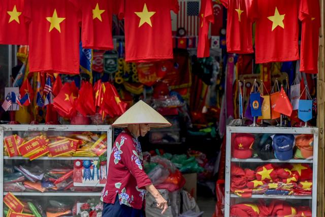A woman walks past a shop selling shirts and flags featuring the Vietnamese national flag in Hanoi on August 28, 2026. (Photo by Nhac NGUYEN / AFP)