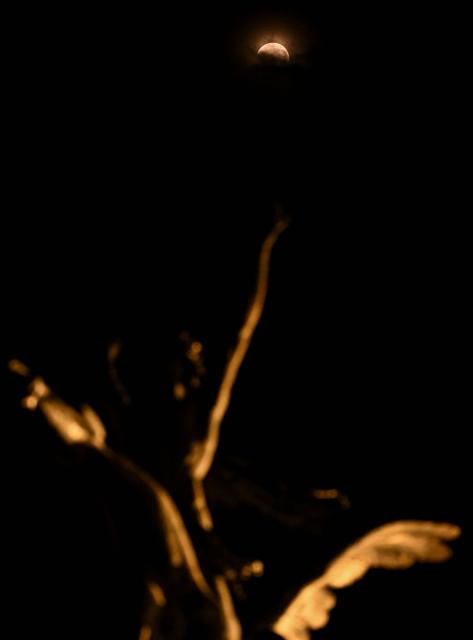 The moon turns red during a partial lunar eclipse over a statue at the Palace of Fine Arts in Mexico City on August 27, 2026. (Photo by Yuri CORTEZ / AFP)
