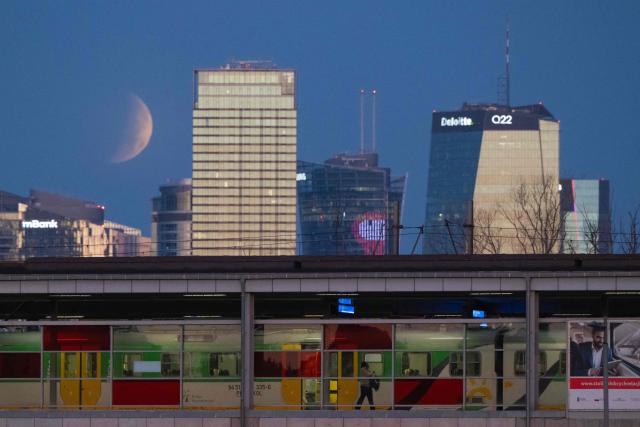A passenger gets off a train as the full moon, also known as the Sturgeon Moon, sets over Warsaw's skyscrapers and the Vistula River during a partial lunar eclipse in Warsaw on August 28, 2026. (Photo by Sergei GAPON / AFP)