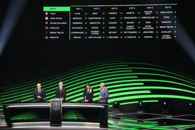 This photograph shows a screen displaying pot 6 fixtures for the league phase of the 2026-2027 UEFA Conference League football tournament as UEFA Deputy General Secretary Giorgio Marchetti (L), Turkish former footballer Metin Tekin (2nd L) and hosts Becky Ives (2nd R) and Matt Smith (R) attend the draw ceremony at the Grimaldi Forum in the Principality of Monaco on August 28, 2026. (Photo by Valery HACHE / AFP)