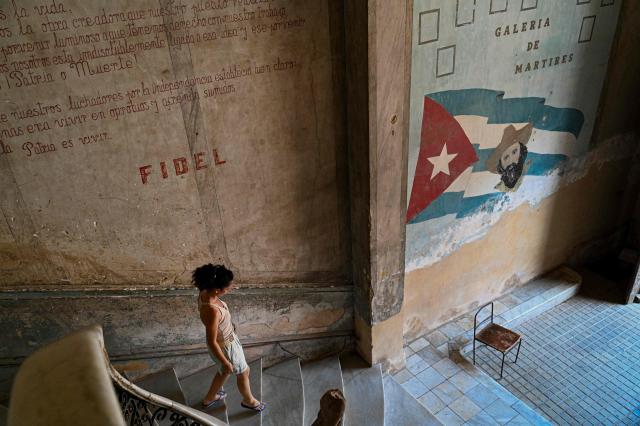 A person descends a staircase lined with revolutionary-themed paintings at La Guarida restaurant, one of Cuba's best-known restaurants internationally, located in the Havana building featured in the Cuban film "Strawberry and Chocolate" ("Fresa y Chocolate"), on August 21, 2026. Opening a restaurant in today's Cuba defies all logic. Amid power outages, shortages of supplies and a sharp decline in tourism, some Cubans keep their businesses open while others even take the risk of launching new establishments. (Photo by ADALBERTO ROQUE / AFP)