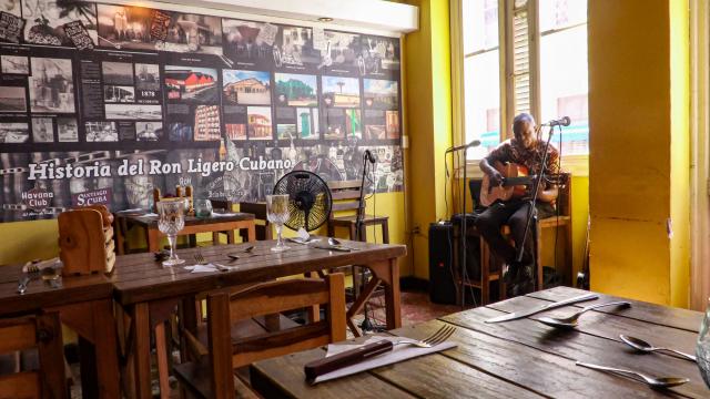A musician performs beside empty tables at El Balcon de los Hermanos restaurant in Havana on August 22, 2026. Opening a restaurant in today's Cuba defies all logic. Amid power outages, shortages of supplies and a sharp decline in tourism, some Cubans keep their businesses open while others even take the risk of launching new establishments. (Photo by ADALBERTO ROQUE / AFP)