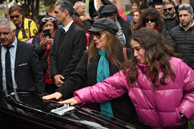 Uruguayan singer and songwriter Ruben Rada's widow Patricia Jodara Leizerovich (C), touches his coffin during his funeral at the cemetery in Montevideo on August 28, 2026. The popular Uruguayan musician and composer Ruben Rada died on August 26, 2026 at the age of 83 from pneumonia, according to an announcement by the family of the artist who fused candombe with rock and jazz. (Photo by EITAN ABRAMOVICH / AFP)