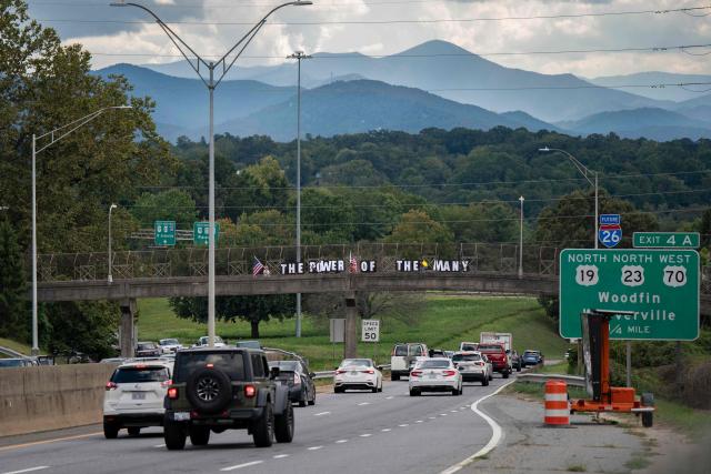 People hold signs reading "the power of the many" on a freeway overpass as they protest ahead of the G20 Finance ministers and central bank governors meeting on August 28, 2026, in Asheville, North Carolina. Asheville is hosting the G20 meetings from August 29 to September 1. (Photo by Allison Joyce / AFP)