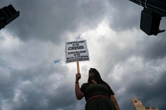 A person holds a sign reading "capitalism is the crisis, socialism is the solution" as they protest ahead of the G20 Finance ministers and central bank governors meeting on August 28, 2026, in Asheville, North Carolina. Asheville is hosting the G20 meetings from August 29 to September 1. (Photo by Allison Joyce / AFP)