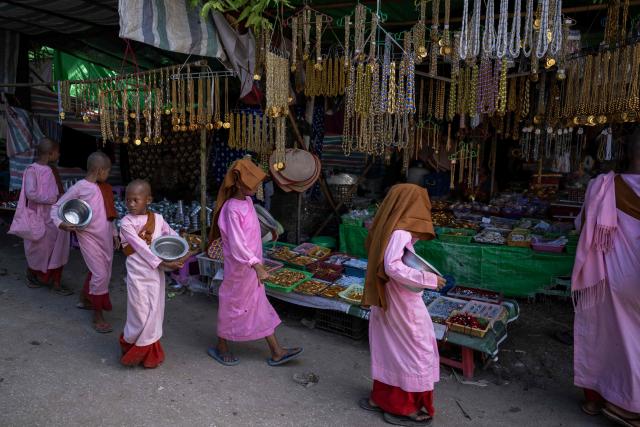 Buddhist nuns walk along market stalls during the annual Taungbyone Spirit Festival in Madaya township, Mandalay region on August 26, 2026. As monsoon rains pound the heartlands of war-fractured Myanmar, "spirit consorts" gather to renew their vows with a pantheon of gods hailed for their powers to protect and destroy. (Photo by SAI AUNG MAIN / AFP) / TO GO WITH AFP STORY: Myanmar-religion-festival-conflict, FOCUS