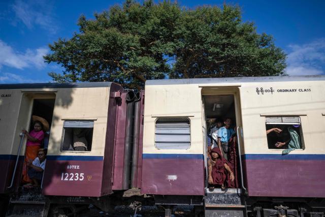 Devotees stand near by open doorway inside a crowded commuter train travelling between Mandalay and Taungbyone for the annual Taungbyone Spirit Festival in Madaya township, Mandalay region on August 26, 2026. As monsoon rains pound the heartlands of war-fractured Myanmar, "spirit consorts" gather to renew their vows with a pantheon of gods hailed for their powers to protect and destroy. (Photo by SAI AUNG MAIN / AFP) / TO GO WITH AFP STORY: Myanmar-religion-festival-conflict, FOCUS
