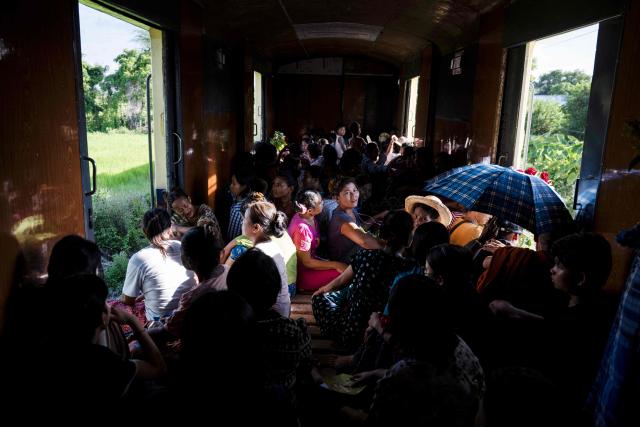 Devotees sit near open doorways inside a crowded commuter train travelling between Mandalay and Taungbyone for the annual Taungbyone Spirit Festival in Madaya township, Mandalay region on August 26, 2026. As monsoon rains pound the heartlands of war-fractured Myanmar, "spirit consorts" gather to renew their vows with a pantheon of gods hailed for their powers to protect and destroy. (Photo by SAI AUNG MAIN / AFP) / TO GO WITH AFP STORY: Myanmar-religion-festival-conflict, FOCUS