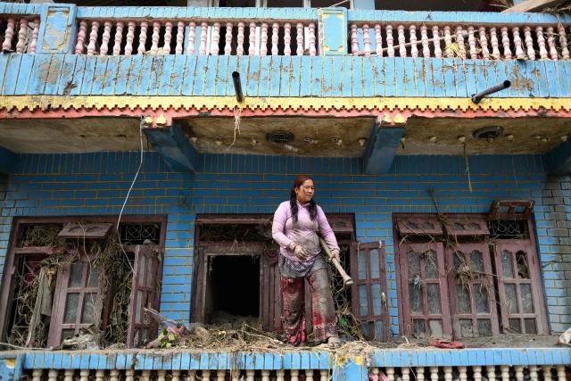 A woman clears debris from her house heavily covered in mud following flash floods at Devighat in Nepal's Nuwakot district on August 29, 2026. Rescuers in Nepal and China were still battling August 29 to locate thousands of people missing days after a deadly, tsunami-like wall of water and debris swept through the Himalayan region, engulfing villages. The number of missing soared past 2,400 on August 28 as emergency teams said they had recovered 623 bodies -- with some of the dead possibly swept downstream as far away as India. (Photo by Manan VATSYAYANA / AFP)