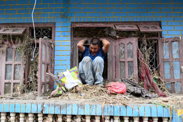 A man climbs out of a window after searching for his belongings inside his house heavily covered in mud following flash floods at Devighat in Nepal's Nuwakot district on August 29, 2026. Rescuers in Nepal and China were still battling on August 29 to locate thousands of people missing days after a deadly, tsunami-like wall of water and debris swept through the Himalayan region, engulfing villages. Nearly 3,000 people were still missing on August 29 and 633 confirmed dead after flash floods and landslides hit the Nepal-Tibet border. (Photo by Manan VATSYAYANA / AFP)