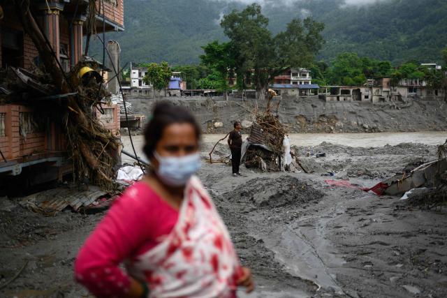 A man (R) stands amidst houses heavily covered in mud following flash floods at Devighat in Nepal's Nuwakot district on August 29, 2026. Rescuers in Nepal and China were still battling on August 29 to locate thousands of people missing days after a deadly, tsunami-like wall of water and debris swept through the Himalayan region, engulfing villages. Nearly 3,000 people were still missing on August 29 and 633 confirmed dead after flash floods and landslides hit the Nepal-Tibet border. (Photo by Manan VATSYAYANA / AFP)