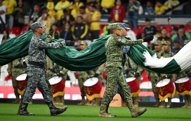 Members of the Mexican armed forces carry a Mexican flag during a tribute and recognition ceremony for their work during the recent FIFA World Cup, before the start of the Liga MX Apertura tournament football match between America and Puebla, at the Bannorte stadium in Mexico City, on August 29, 2026. (Photo by YURI CORTEZ / AFP)