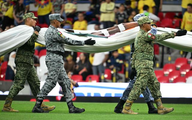Members of the Mexican armed forces carry a Mexican flag during a tribute and recognition ceremony for their work during the recent FIFA World Cup, before the start of the Liga MX Apertura tournament football match between America and Puebla, at the Bannorte stadium in Mexico City, on August 29, 2026. (Photo by YURI CORTEZ / AFP)