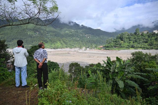People look at the mud-inundated Trishuli river at Trishuli Center in Nepal's Nuwakot district on August 30, 2026, after catastrophic flooding on the Nepal-Tibet border. The number of people missing in the catastrophic flood that sliced through the border area between Nepal and Tibet neared 3,000 on August 30, as rescuers scoured deep, leg-sucking mud for survivors. (Photo by Arun SANKAR / AFP)