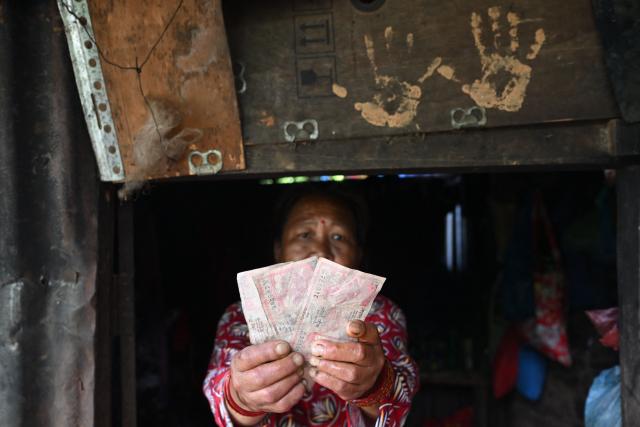 A resident holds up mud-covered Nepali currency at her dwelling beside the Trishuli river at Trishuli Center in Nepal's Nuwakot district on August 30, 2026, after catastrophic flooding on the Nepal-Tibet border. The number of people missing in the catastrophic flood that sliced through the border area between Nepal and Tibet neared 3,000 on August 30, as rescuers scoured deep, leg-sucking mud for survivors. (Photo by Arun SANKAR / AFP)