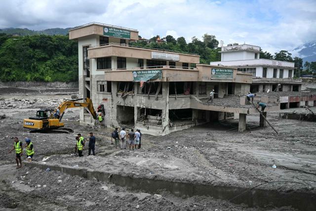 A team of Nepal police and the National Disaster Risk Reduction and Management Authority (NDRRMA) uses an excavator (L) to retrieve money and documents from a bank covered in sludge in the aftermath of flash floods at Trishuli in Nepal's Nuwakot district on August 30, 2026. The number of people missing in the catastrophic flood that sliced through the border area between Nepal and Tibet neared 3,000 on August 30, as rescuers scoured deep, leg-sucking mud for survivors. (Photo by Arun SANKAR / AFP)