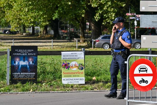 Police officers secure the area next to a poster advertising a rave where a shooting occurred, in Aarau, northern Switzerland, on 30 August 2026. One person was killed and five others were wounded, some of them seriously, in a shooting at a rave party in northern Switzerland, local police said. (Photo by Harold CUNNINGHAM / AFP)