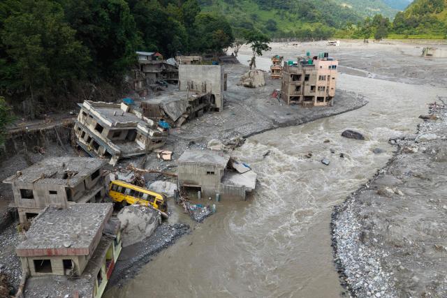 An aerial view shows a torrent of muddy water surging past houses and through the Trishuli river in the aftermath of flash floods, at Betrawati in Nepal's Nuwakot district on August 29, 2026. More than 3,000 people were listed as missing on August 30, with another 768 confirmed dead, after the flash floods and landslides that hit the Nepal-Tibet border. (Photo by PRABIN RANABHAT / AFP)