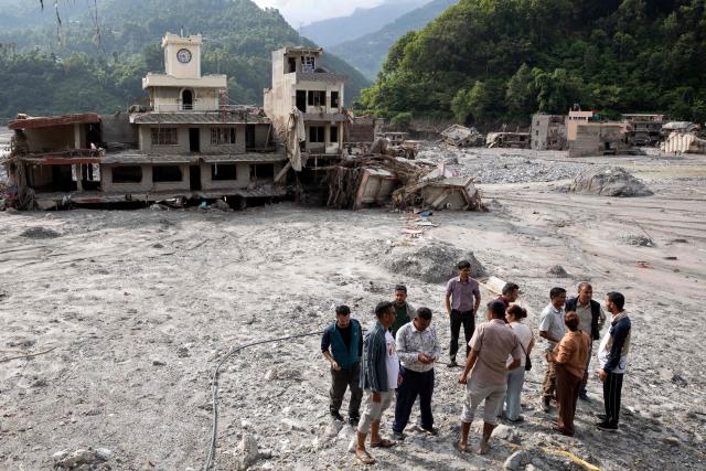 People stand near houses deluged in sludge in the aftermath of flash floods, along the Trishuli river at Betrawati in Nepal's Nuwakot district on August 29, 2026. More than 3,000 people were listed as missing on August 30, with another 768 confirmed dead, after the flash floods and landslides that hit the Nepal-Tibet border. (Photo by PRABIN RANABHAT / AFP)